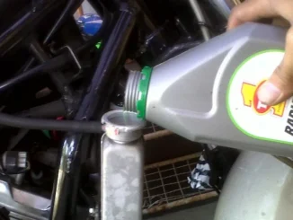 Menuang cairan radiator coolant dari botol ke lubang pengisian radiator motor
