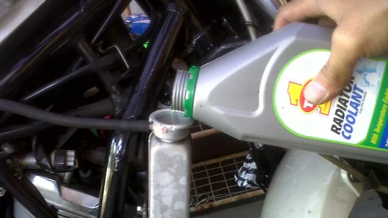 Menuang cairan radiator coolant dari botol ke lubang pengisian radiator motor
