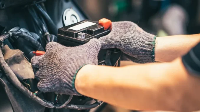 Tangan bersarung tangan melepas aki dari rumah aki sepeda motor