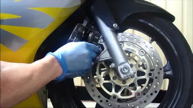 Tangan bersarung tangan memegang kaliper rem depan di samping cakram motor sport kuning