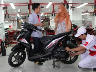 Mekanik berseragam Honda mengerjakan roda belakang Honda Beat hitam di bengkel resmi