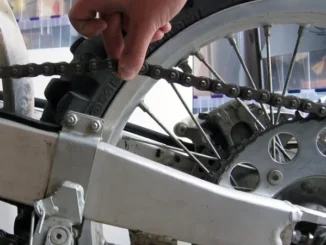 Tangan memeriksa ketegangan rantai pada roda belakang motor berpelek jari-jari
