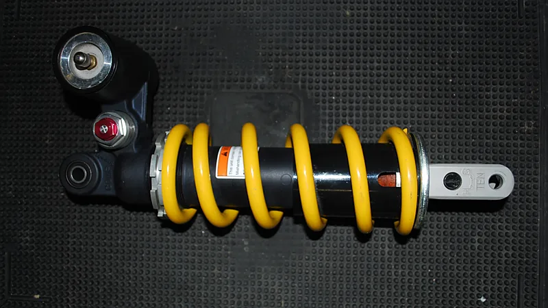 Shockbreaker monoshock dengan per kuning dan ring penyetel preload, difoto terlepas di atas alas karet