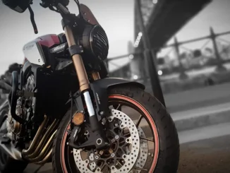 Garpu depan upside down emas Honda CB650R dengan cakram depan dan tulisan ABS di kakinya, berlatar jembatan