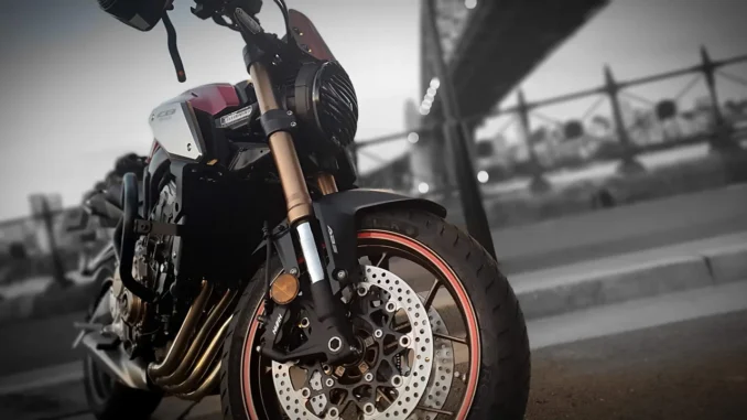Garpu depan upside down emas Honda CB650R dengan cakram depan dan tulisan ABS di kakinya, berlatar jembatan