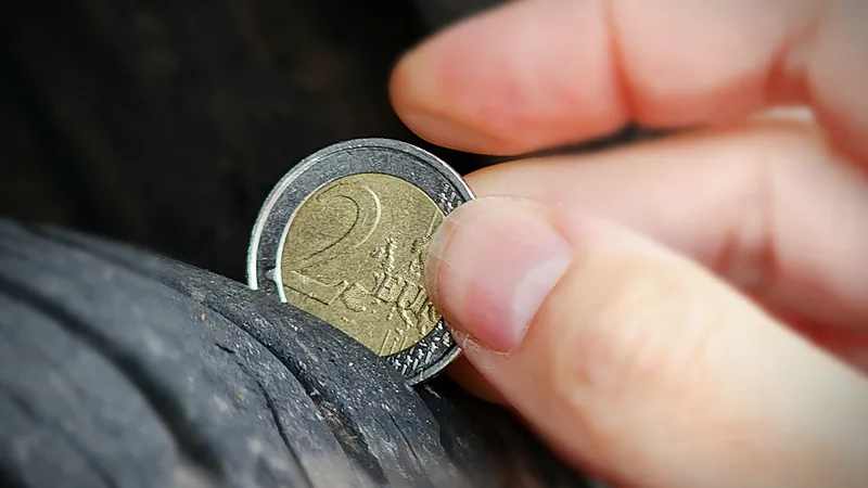 Tangan menekan koin dua euro ke alur ban untuk mengecek kedalaman tapak yang mulai aus
