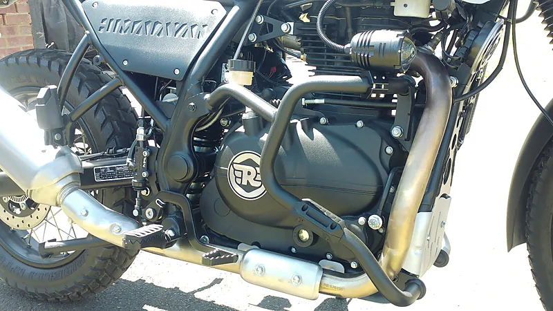 Lampu tembak kecil berbodi krom terpasang pada crash bar Royal Enfield Himalayan, di samping blok mesin dan leher knalpot