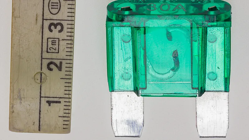 Sekring tancap blade fuse berwarna hijau bertanda 30A diletakkan di samping penggaris, tinggi sekitar 3 sentimeter