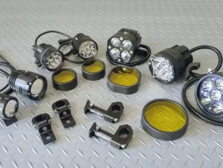 Delapan unit lampu tembak LED motor dengan kabel spiral, braket jepit setang, dan tutup filter kuning, tertata di atas pelat bordes