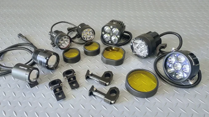 Delapan unit lampu tembak LED motor dengan kabel spiral, braket jepit setang, dan tutup filter kuning, tertata di atas pelat bordes