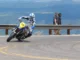 Pembalap supermoto bernomor 43 merebahkan motornya di tikungan aspal pegunungan dengan pembatas jalan di belakangnya