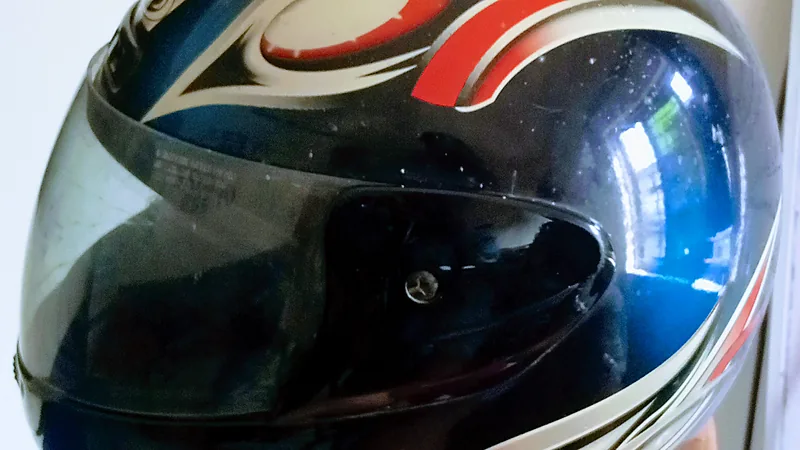 Visor gelap helm motor sport dalam posisi tertutup, dengan baut engselnya terlihat di sisi helm