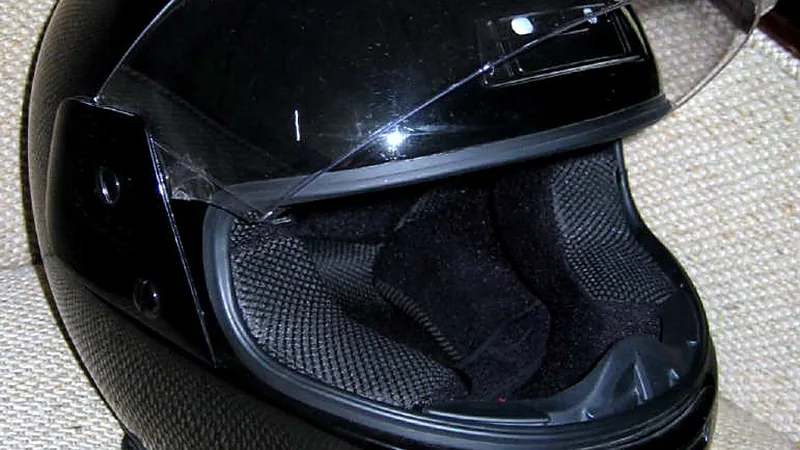 Helm full-face hitam dengan visor bening terangkat, memperlihatkan lapisan dalam dan bantalan pipinya