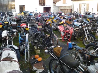Halaman bengkel penuh motor tua yang terparkir bertumpuk dan berdebu, sebagian tinggal rangka