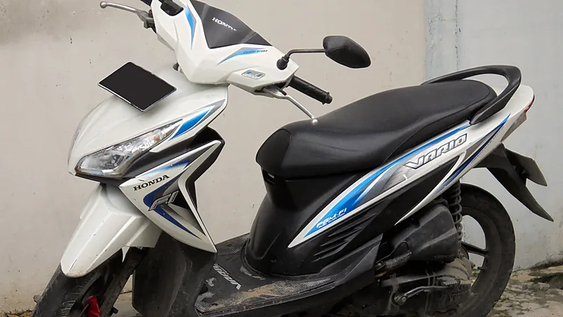 Honda Vario FI putih-biru dengan lencana PGM-FI terparkir menyamping di depan tembok