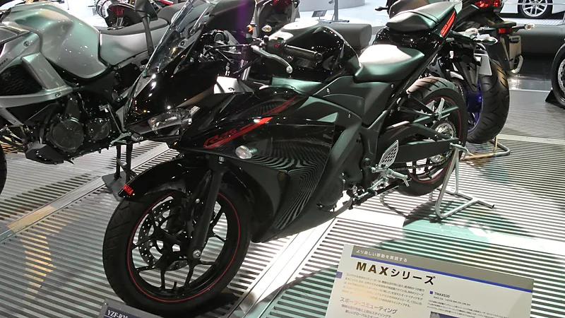Yamaha YZF-R25 hitam dipajang di lantai pameran, terlihat dari sisi depan-kiri dengan fairing dan pelek berlis merah