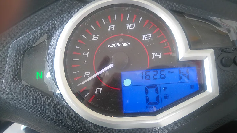 Panel meter motor dengan takometer analog dan layar LCD digital biru yang menampilkan odometer, posisi gigi netral, dan indikator bensin