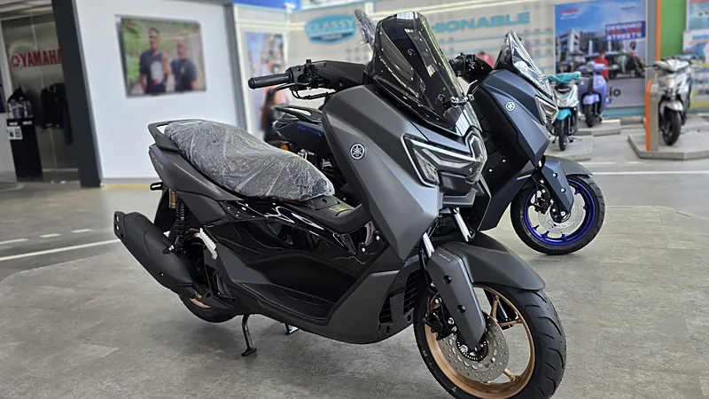 Dua Yamaha NMax abu-abu doff dipajang di ruang pamer dealer, jok masih terbungkus plastik dan lampu depan LED menghadap kamera