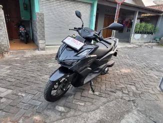 Honda Vario 160 hitam berpelat dealer merah diparkir di gang paving blok, tampak depan-samping