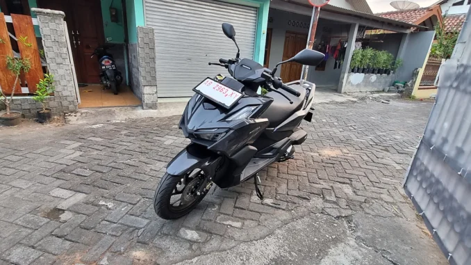 Honda Vario 160 hitam berpelat dealer merah diparkir di gang paving blok, tampak depan-samping