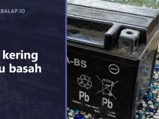 Aki motor tipe kering tersegel dari dekat dengan tanda daur ulang dan peringatan jangan dibuka di badannya, dengan panel judul Aki kering atau basah di sisi kiri