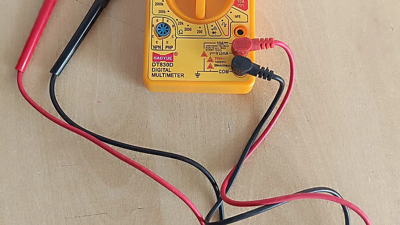 Multimeter digital DT830D warna kuning dengan probe merah dan hitam terpasang di lubang COM dan V-ohm-mA