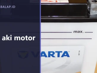Aki motor tipe basah dari dekat dengan terminal di bagian atas dan garis batas min serta max di badannya, dengan panel judul Cas aki motor di sisi kiri