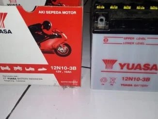 Aki sepeda motor basah Yuasa 12N10-3B 12 volt 10 Ah berdiri di samping kotak kemasannya