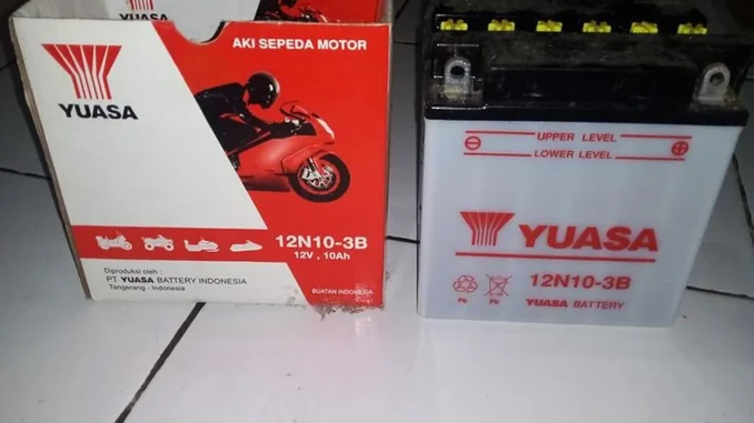Aki sepeda motor basah Yuasa 12N10-3B 12 volt 10 Ah berdiri di samping kotak kemasannya