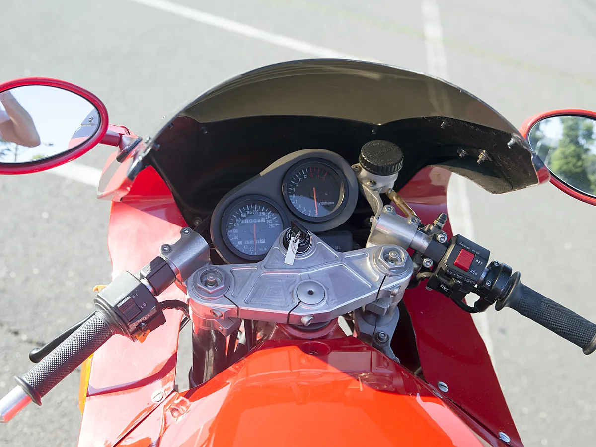 Panel instrumen motor sport merah dari posisi pengendara, spidometer dengan jendela odometer di sebelah kiri takometer, di antara dua spion bulat