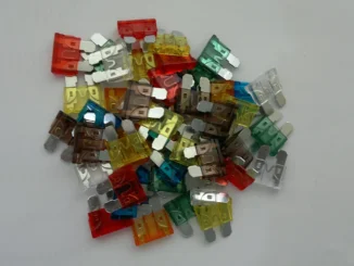 Tumpukan sekring blade berbagai warna - merah, cokelat, kuning, biru, hijau, oranye, dan bening - di atas permukaan putih