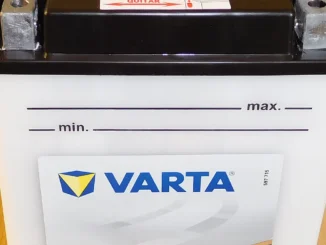 Aki motor basah merek Varta warna putih dengan dua terminal logam di atas dan garis penanda batas air min dan max di badannya