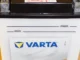 Aki motor basah merek Varta warna putih dengan dua terminal logam di atas dan garis penanda batas air min dan max di badannya